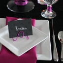 A simple black place card written in silver letters with a pink wire stand.