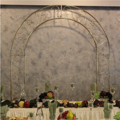 A tall brass arch is placed behind an ivory bridal table. The table is decorated with tall candle-filled centerpieces and sage green accents.